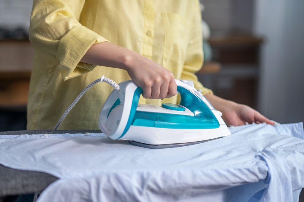 cropped photo of a woman smoothing out wrinkles on the shirt with a steam iron